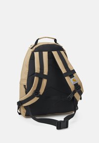 Mochila bege e preta com alças acolchoadas, múltiplos compartimentos, um emblema e um design robusto adequado para uso diário.