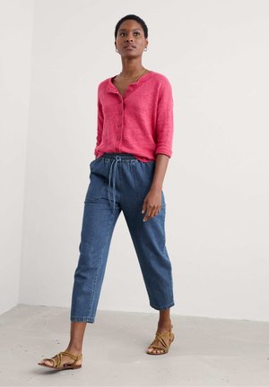 Pink linen button-up top with three-quarter sleeves, paired with blue drawstring trousers and brown strappy sandals. Simple design.
