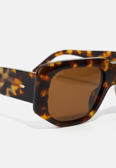 Tortoiseshell sunglasses with a chunky square frame, brown lenses, and logo detail on the side; glossy plastic finish with a textured pattern.