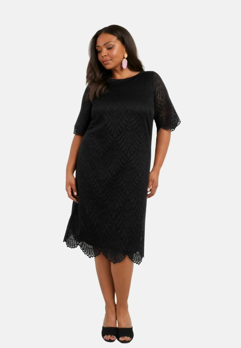 Černé krajkové šaty s krátkými širokými rukávy a zubatým lemem, zdobené texturovaným vzorem. Kombinované s černými sandály na otevřenou špičku.