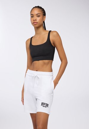 Top corto nero abbinato a pantaloni corti bianchi con cordoncino, caratterizzati dalla scritta "NEW YORK USA '96" stampata in nero. Tessuto liscio, design casual.