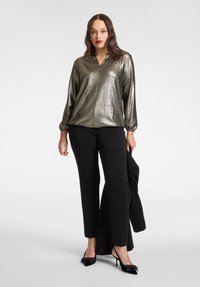 Blusa argento metallizzato con scollo a V, polsini elasticizzati e vestibilità morbida, abbinata a pantaloni neri e tacchi neri alla moda.