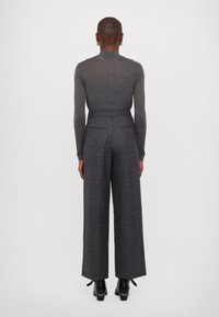 Hellgraues, transparentes Langarmtop, kombiniert mit dunkelgrauen, karierter weit geschnittenen Hose. Die Hose hat einen taillierten Bund und Gesäßtaschen.