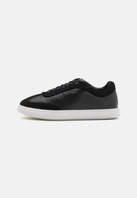 Sneaker in pelle nera e suede con suola in gomma bianca, punta rotonda e design con lacci; presenta un branding minimalista di lato.