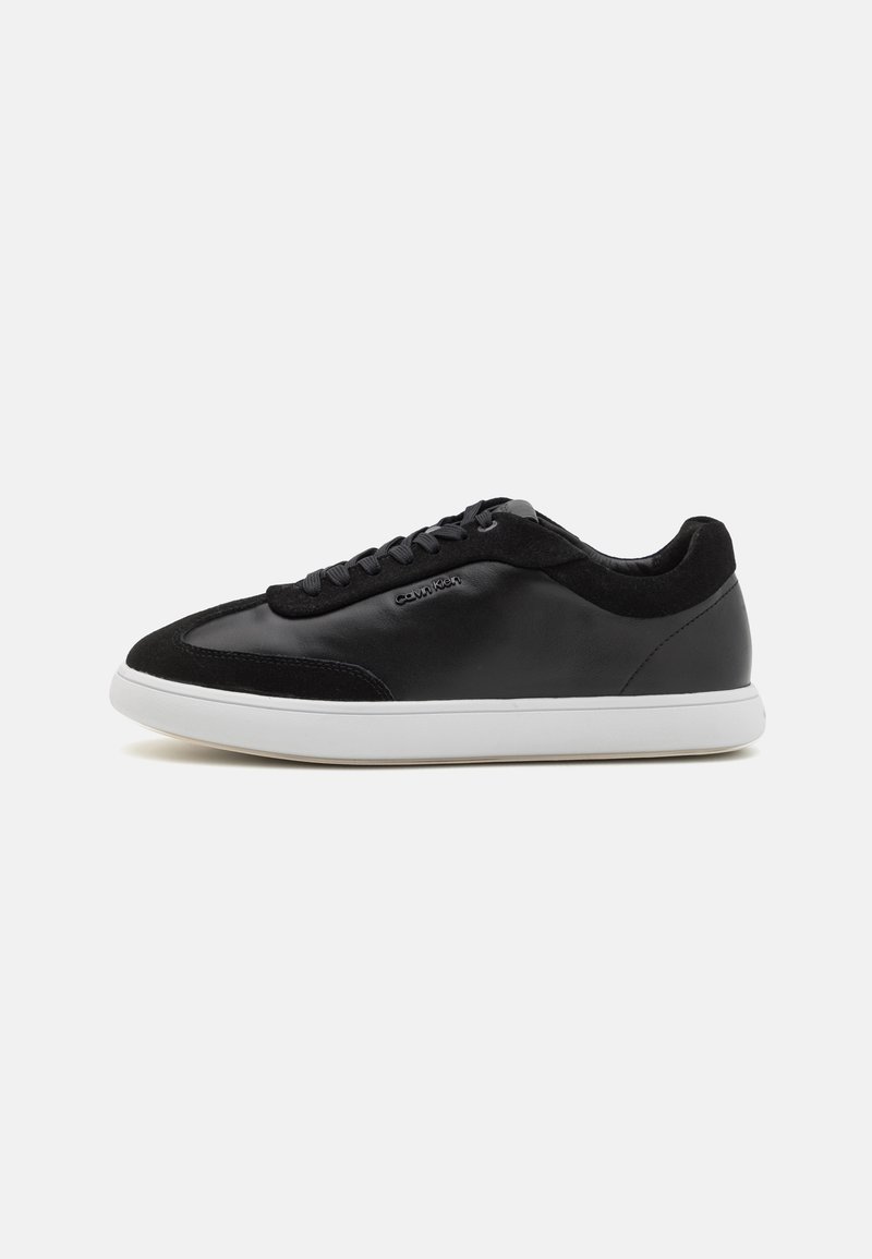 Sneaker in pelle nera e suede con suola in gomma bianca, punta rotonda e design con lacci; presenta un branding minimalista di lato.
