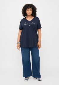 Navy t-skjorte med «love is love» trykket i hvit skrift. Korte ermer, rund halslinje, løs passform. Kombinert med vide blå jeans.