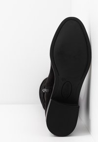Schwarzer Wildleder-Ankle-Boot mit einer strukturierten Gummisohle, seitlichem Reißverschluss und runder Zehenform, der eine glatte, straffe Silhouette präsentiert.