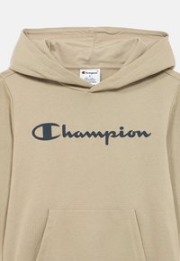 Μπεζ φούτερ με κουκούλα από απαλό ύφασμα, με μπροστινή τσέπη και γκρι λογότυπο με την επιγραφή "Champion" στο στήθος. Πυκνή υφή πλεκτού.