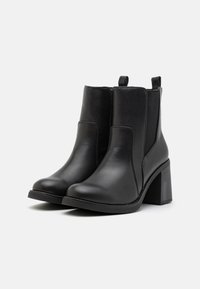 Botas de tobillo de cuero negro con puntera redondeada, tacón cuadrado medio, paneles elásticos en los laterales y acentos texturizados en la parte superior.