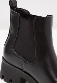 Czarne botki za kostkę z gładkiej skóry, elastycznymi bocznymi panelami i masywną, wyprofilowaną podeszwą. Posiadają pętelkę z tyłu.