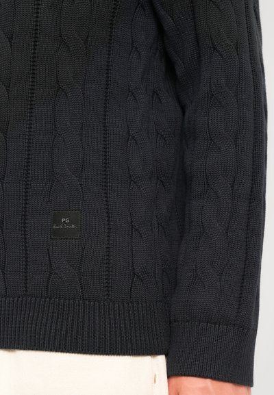 Σκούρο ναυτικό μπλε πουλόβερ με κόμπους στην πλέξη, μανίκι και κάτω μπροστινό μέρος με ριμπ μανσέτα και ποδόγιλο, μικρή μαύρη ετικέτα που γράφει "PS Paul Smith" κοντά στο ποδόγιλο.