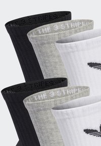 Drei Paar Sneakersocken in Schwarz, Grau und Weiß mit einer gerippten Textur und einem kontrastierenden Bündchen, das das "THE 3 STRIPES"-Logo in Schwarz und Weiß zeigt.