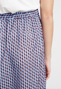 Gonna stampata con vita elastica, caratterizzata da un design geometrico in blu, marrone e nero su uno sfondo chiaro. Tessuto dalla consistenza liscia.