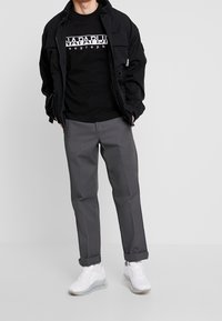 Black zip-up jacket, black graphic t-shirt, gray tapered pants, and white sneakers. Features include pockets on the jacket and rolled pant cuffs.