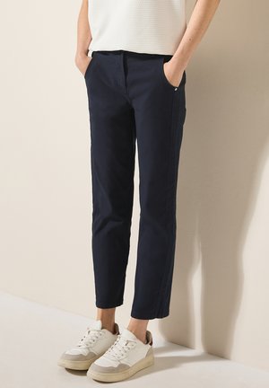 Pantaloni blu navy con vestibilità dritta, dotati di tasche laterali e aperture delle gambe strette, abbinati a sneakers bianche e beige.