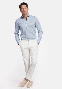 Chemise bleue claire à manches longues avec de petits motifs, pantalon blanc et chaussures à enfiler beiges. Design slim fit mettant en valeur une silhouette épurée.