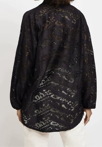 Top in pizzo nero con tessuto testurizzato e vestibilità ampia. Caratterizzato da maniche lunghe e un motivo ondulato, con un retro leggermente più lungo e orlo arrotondato.