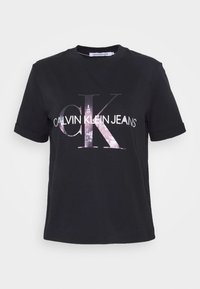 Black cotton T-shirt with a crew neck, short sleeves, and a large graphic print of "CALVIN KLEIN JEANS" and "CK" in metallic pink on the front.