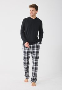 Chemise noire à manches longues avec un col henley associée à un pantalon de pyjama à carreaux gris et noirs, doté d'une taille élastique et d'une coupe décontractée.
