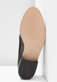 Czarna podeszwa buta z gładką beżową powierzchnią, posiadająca żeberkowaną teksturę na pięcie oraz wytłoczone napisy: "MADE IN SPAIN 37."