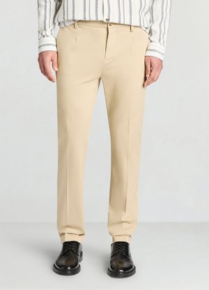 Beige maßgeschneiderte Hose mit glatter Textur, scharfen Bügelfalten und Seitentaschen, kombiniert mit schwarzen Lederschuhen für einen Kontrast.