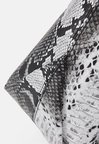 Borsa a tracolla con stampa a serpente in bianco e nero, con superficie testurizzata, forma angolare e squame a contrasto. Dettaglio di cucitura visibile lungo le cuciture.