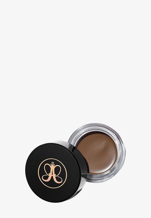 Bruin crèmeproduct in een ronde, doorzichtige glazen pot met een zwarte deksel. De deksel heeft een logo in reliëf in roségoud. Zachte textuur zichtbaar aan de binnenkant.