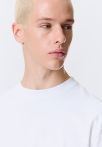 Hvid bomulds t-shirt med rund hals. Nærbillede af ansigt med blondt hår og neutral udtryk. Blød tekstur, minimalistisk design.