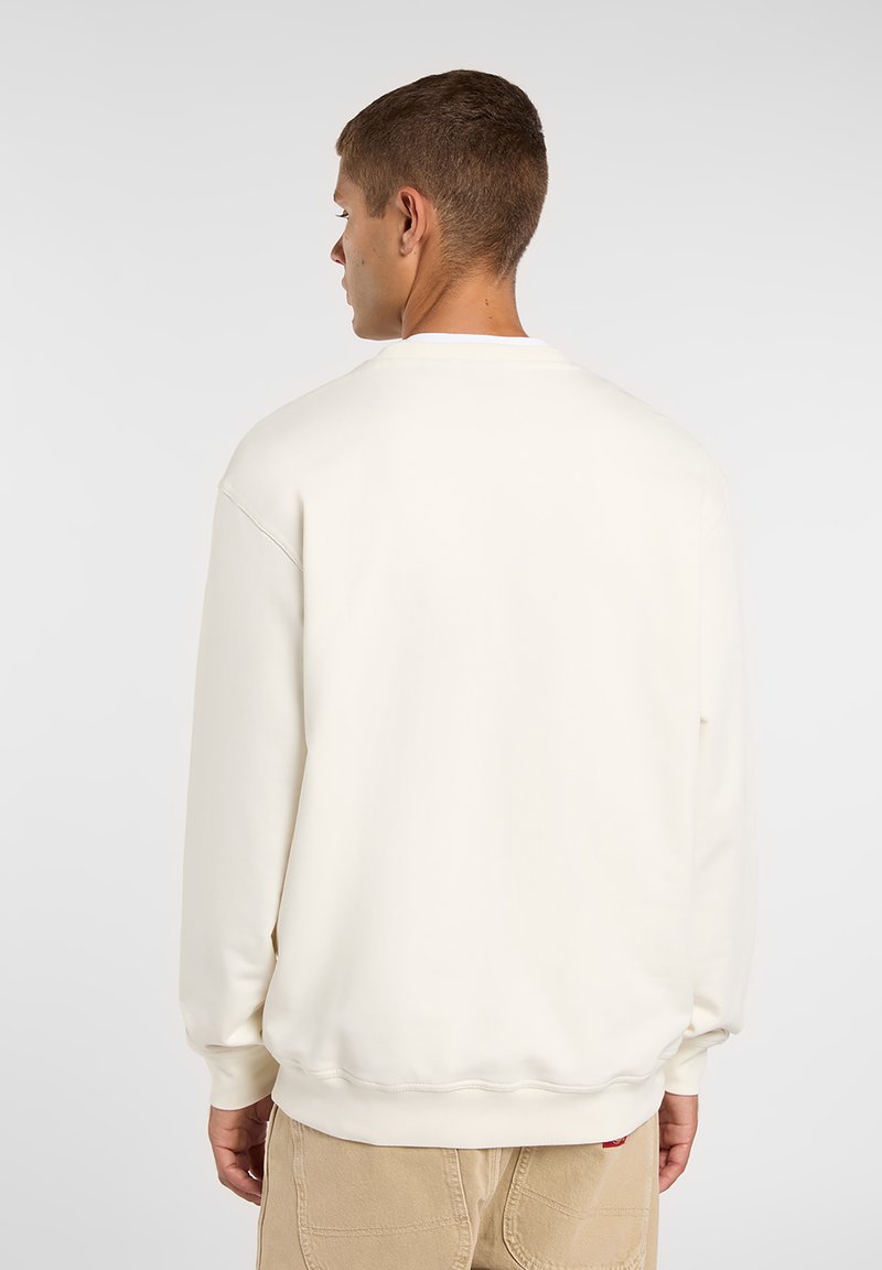 Sudadera de color crema con textura suave, cuello redondo y puños acanalados. Se lleva con pantalones beige. Diseño sencillo, sin logotipos visibles.