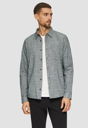 Knoop-overhemd in een blauw en grijs textuurpatroon, met lange mouwen en een klassieke kraag. Gecombineerd met een wit T-shirt eronder.