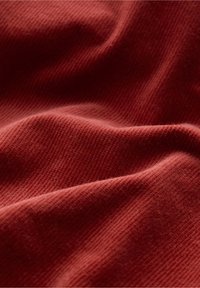 Tissu rouge texturé avec un motif côtelé, présentant des ondulations et des plis doux, suggérant une texture chaude et confortable adaptée aux vêtements ou à la tapisserie.