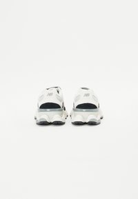 Sneakers with a white mesh and suede upper, featuring a black accent, chunky sole, and transparent heel detail. Plain white background.