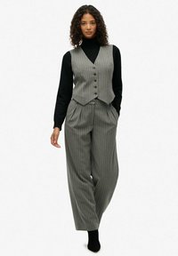 Szary i biały kamizelka w paski z guzikami, w połączeniu z dopasowanymi spodniami z wysokim stanem i szerokimi nogawkami, noszona na czarnym golfie.