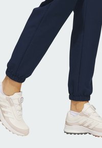 Hvide og lyserøde træningssko med en glat tekstur, gummisål og justerbart BOA-fit system. Sammen med navy joggingbukser.