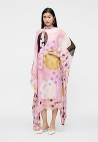 Priehľadný ružový kaftan s veľkými farebnými bodkami, splývavé rukávy a zodpovedajúca stužka na krk. Ľahká látka s hladkým povrchom.