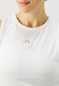 Λευκό αθλητικό κανονάκι με στρογγυλή λαιμόκοψη και διακριτικό ασημένιο λογότυπο στο στήθος. Λείο, ελαφρύ ύφασμα με εφαρμοστή σχεδίαση.