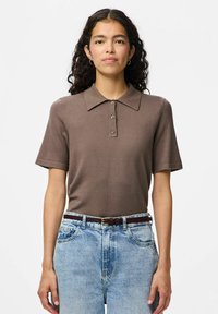 Brun kortärmad polo av stickat tyg med krage och tre knappslå. Matchad med ljusblå högmidjade jeans och ett mörkt bälte.