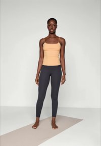 Beige yoga matte med en tynn, tettsittende tank topp med smale stropper, sammen med mørkegrå leggings laget av elastisk stoff.