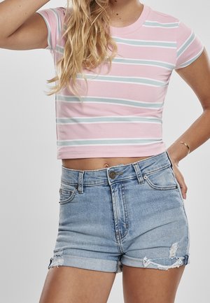 Kobieta ubrana w różowo-biały prążkowany krótki T-shirt i jasnoniebieskie, wysokie dżinsowe szorty z podwiniętymi mankietami i postrzępionymi detalami.