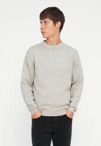 Gray knit sweater with a round neckline and ribbed cuffs, featuring a soft texture and relaxed fit. Worn with black jeans.