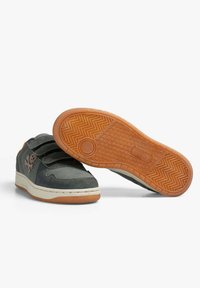 Par de zapatillas oscuras grises y naranjas, una mostrando la parte superior con correas de Velcro, la otra mostrando la suela texturizada de color naranja.