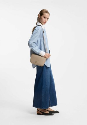 Beige leather crossbody bag with a rectangular shape and minimal hardware, paired with a blue-striped shirt and wide-leg jeans.