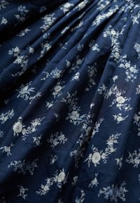 Marineblåt stof med lille hvidt blomsterprint, der viser sammenrullede folder og blød tekstur.