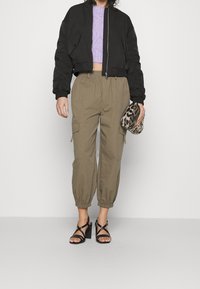 Černá zkrácená bomber bunda, levandulový pletený top, khaki cargo kalhoty se elastickými manžetami, černé sandály na podpatku se řemínky, leopardí vzorovaná kabelka.