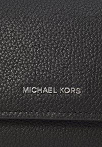 Schwarze Lederhandtasche mit strukturierter Oberfläche und silberfarbener "MICHAEL KORS"-Logo. Schlichte Steppnaht und elegantes Design.