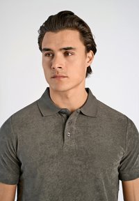 Grijs poloshirt met korte mouwen van textuurstof, met een kraag en een knoopsluiting met drie knopen. Eenvoudig en casual ontwerp.