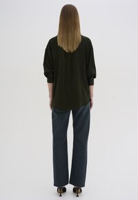 Mørkegrøn oversized skjorte med oprullede ærmer, parret med højtaljede, lige buksedragt i blå denim og sorte højhælede sko.