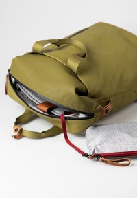 Zaino verde olivastro con una superficie liscia, apertura con zip, dettagli in pelle e un interno caratterizzato da una fodera a quadretti grigia. Include una piccola pochette.