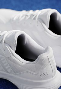 Ζευγάρι λευκά αθλητικά παπούτσια με υφή υφάσματος και κορδόνια σε μπλε επιφάνεια, ορατά από πίσω και από πάνω.