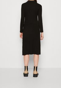 Musta ribbed pitkähihaine mekko kauluksella, leikkaukset sääreen asti, sivu halkioilla, yhdistettynä beigeihin nilkkasaappaisiin ja mustiin sukkiin.